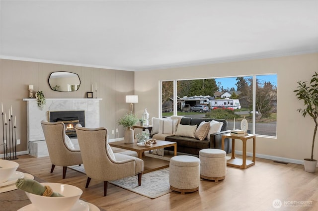 living room with a premium fireplace, visible vents, wood finished floors, and ornamental molding