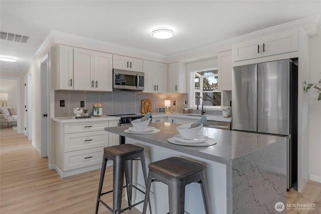 kitchen featuring visible vents, appliances with stainless steel finishes, white cabinetry, and a kitchen breakfast bar