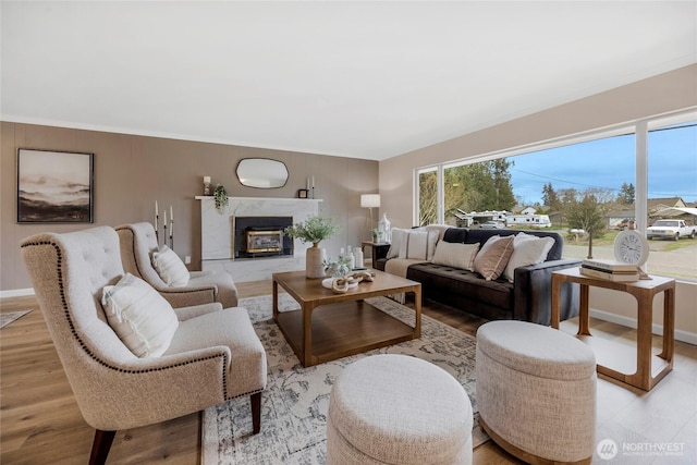 living room with light wood-style flooring, baseboards, a high end fireplace, and ornamental molding