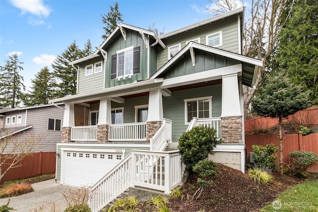 craftsman-style home with stone siding, fence, covered porch, board and batten siding, and a garage