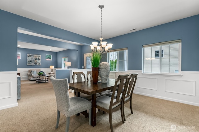 dining room featuring a notable chandelier, visible vents, light colored carpet, and wainscoting