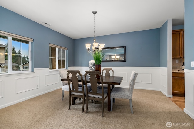 dining space with a wainscoted wall, an inviting chandelier, visible vents, and light carpet