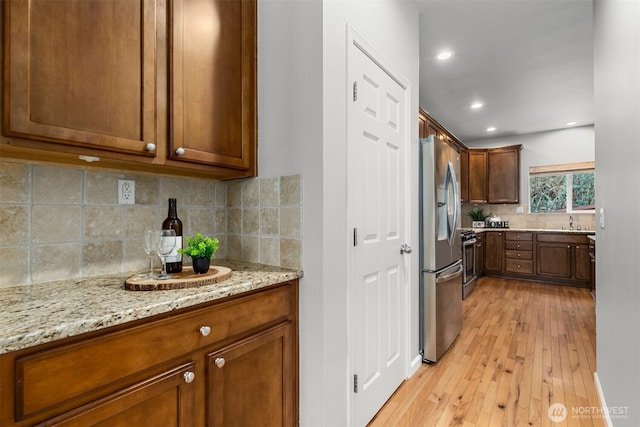 kitchen featuring light wood finished floors, tasteful backsplash, light stone countertops, recessed lighting, and stainless steel refrigerator with ice dispenser