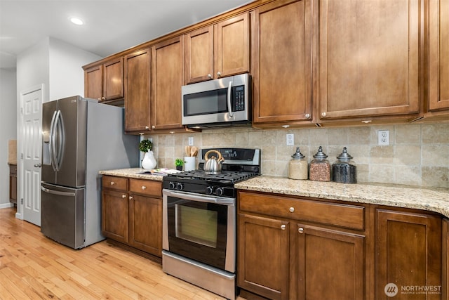 kitchen featuring light wood finished floors, backsplash, appliances with stainless steel finishes, and brown cabinets