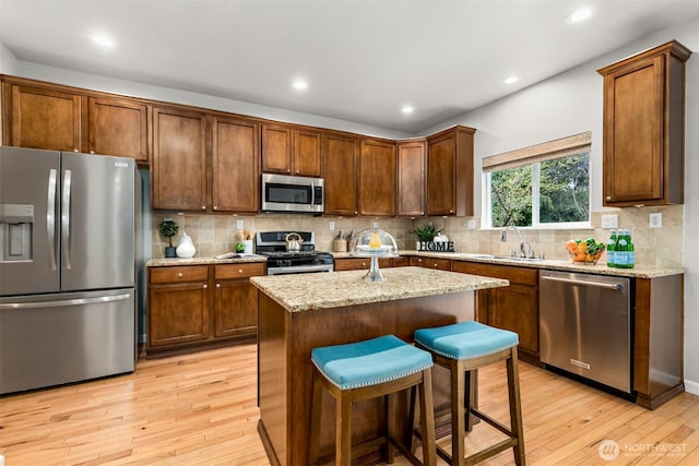 kitchen with tasteful backsplash, light stone countertops, light wood-type flooring, appliances with stainless steel finishes, and a sink