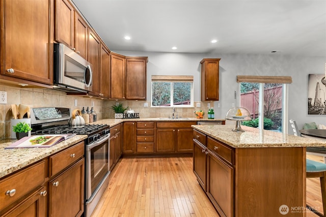 kitchen with a kitchen island, light wood-type flooring, decorative backsplash, stainless steel appliances, and a sink