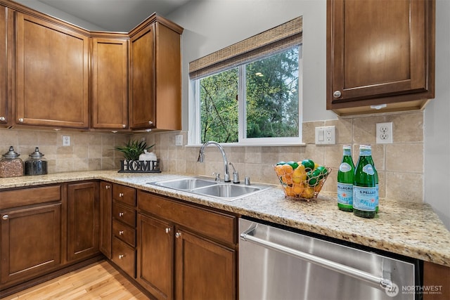 kitchen with light wood finished floors, tasteful backsplash, stainless steel dishwasher, brown cabinetry, and a sink