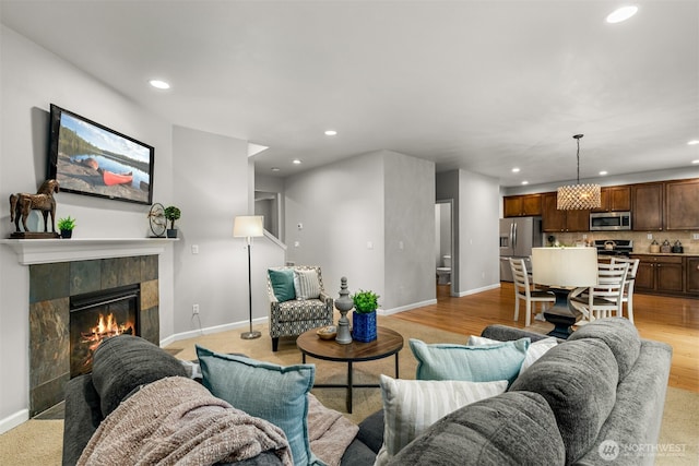 living area featuring a tiled fireplace, recessed lighting, baseboards, and light wood finished floors