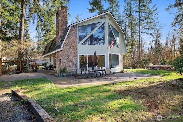 rear view of house with a gambrel roof, a lawn, a chimney, and a patio area