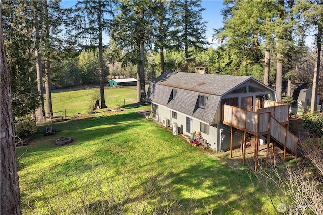 exterior space featuring a wooden deck, a gambrel roof, a lawn, and a shingled roof