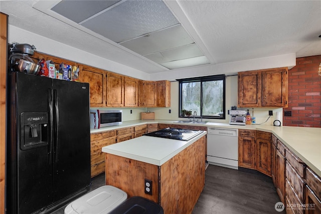 kitchen with stainless steel microwave, dishwasher, black fridge, brown cabinetry, and a sink