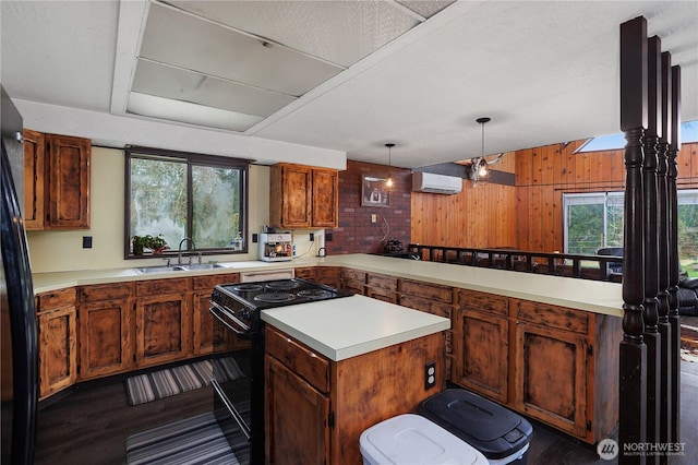 kitchen with a sink, black appliances, light countertops, a wall mounted air conditioner, and a wealth of natural light