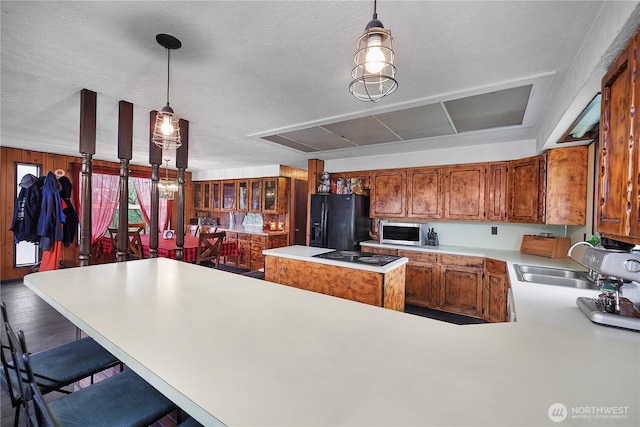 kitchen with a center island, light countertops, brown cabinetry, black appliances, and a sink