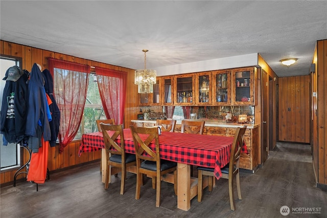 dining area with wooden walls, a notable chandelier, and dark wood-style floors