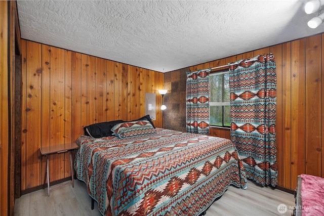 bedroom featuring light wood-style floors, wood walls, and a textured ceiling