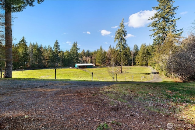 view of yard featuring a rural view, a wooded view, and fence