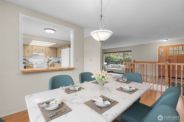 dining space with a textured ceiling, baseboards, and light wood-style floors