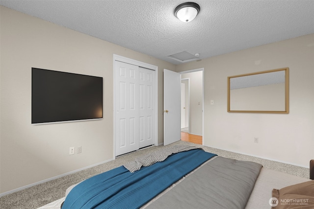 bedroom with a textured ceiling, a closet, carpet, baseboards, and attic access