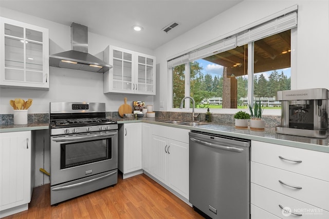 kitchen with visible vents, a sink, stainless steel appliances, light wood-style floors, and wall chimney range hood