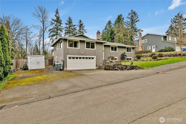 split foyer home featuring an attached garage, a chimney, driveway, and fence