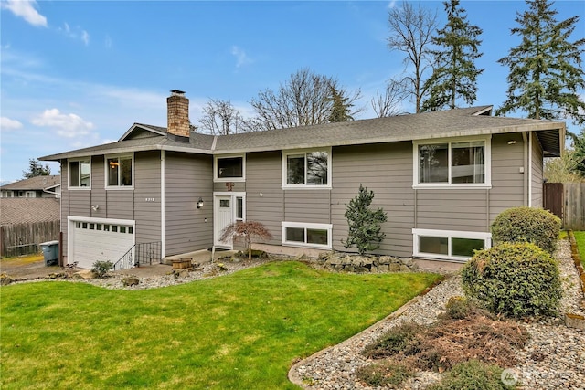 split foyer home featuring a front lawn, an attached garage, fence, and a chimney