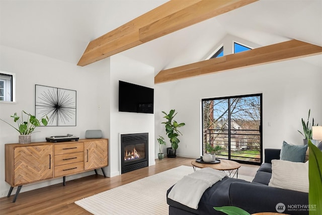 living area with beamed ceiling, wood finished floors, high vaulted ceiling, and a glass covered fireplace