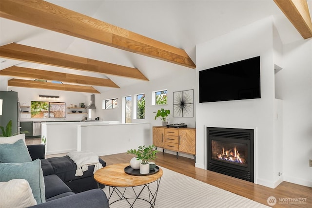 living room featuring a glass covered fireplace, vaulted ceiling with beams, baseboards, and wood finished floors