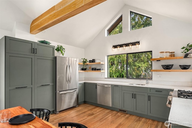 kitchen with light wood finished floors, open shelves, appliances with stainless steel finishes, high vaulted ceiling, and a sink