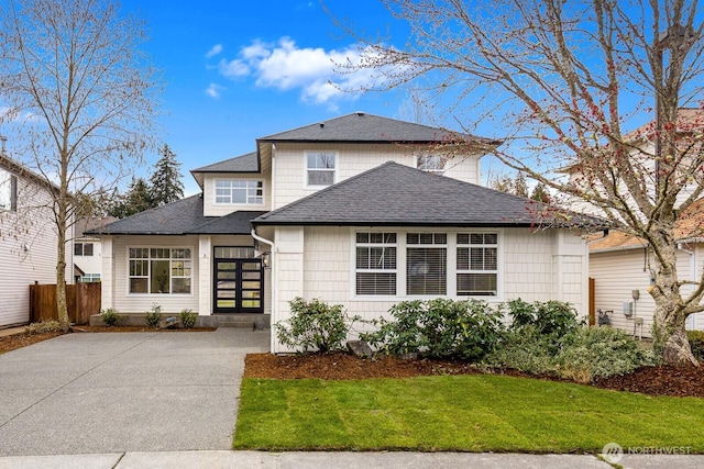 view of front facade featuring a front yard, concrete driveway, fence, and roof with shingles