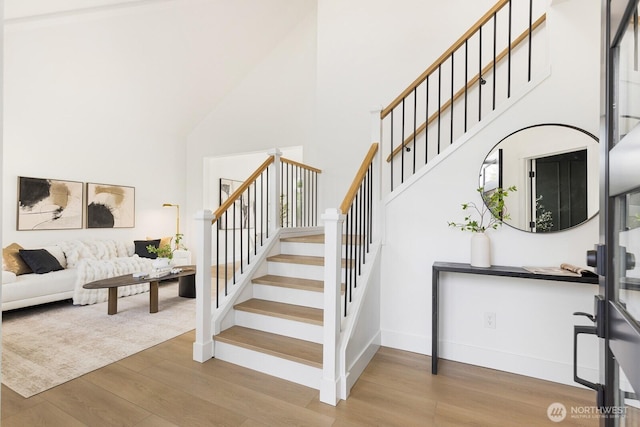 stairway featuring baseboards, a high ceiling, and wood finished floors