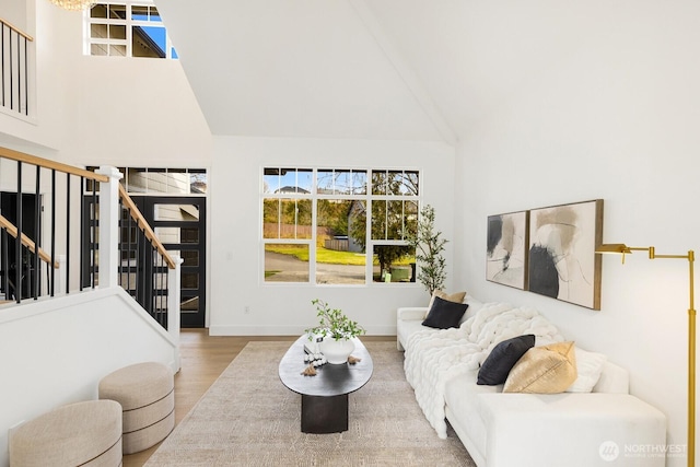 living area with stairway, high vaulted ceiling, baseboards, and wood finished floors