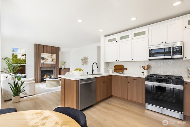 kitchen featuring a sink, appliances with stainless steel finishes, a peninsula, light wood finished floors, and light countertops