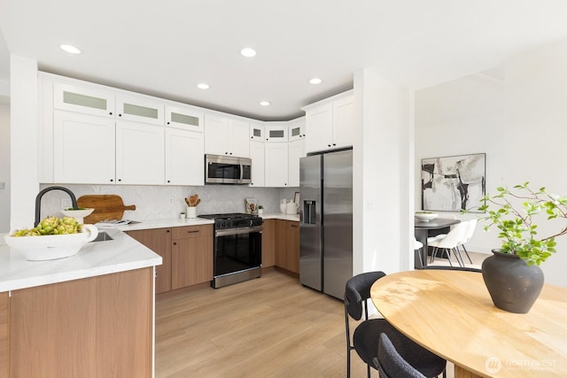 kitchen featuring glass insert cabinets, decorative backsplash, light wood-style flooring, appliances with stainless steel finishes, and a sink