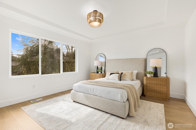 bedroom featuring a tray ceiling, baseboards, visible vents, and wood finished floors