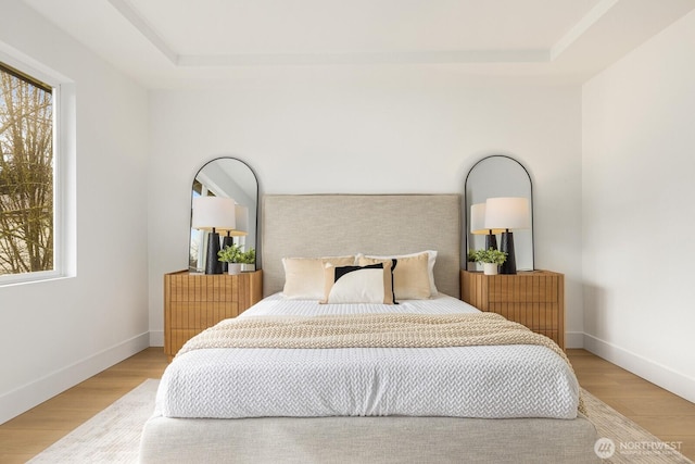 bedroom featuring light wood finished floors, baseboards, and a tray ceiling