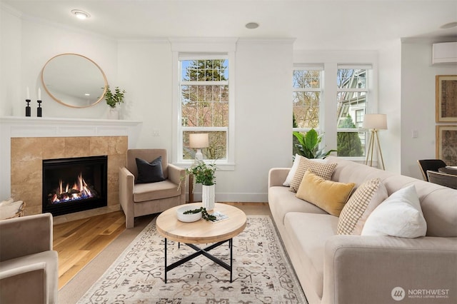 living area with crown molding, baseboards, a wall mounted air conditioner, a tile fireplace, and wood finished floors