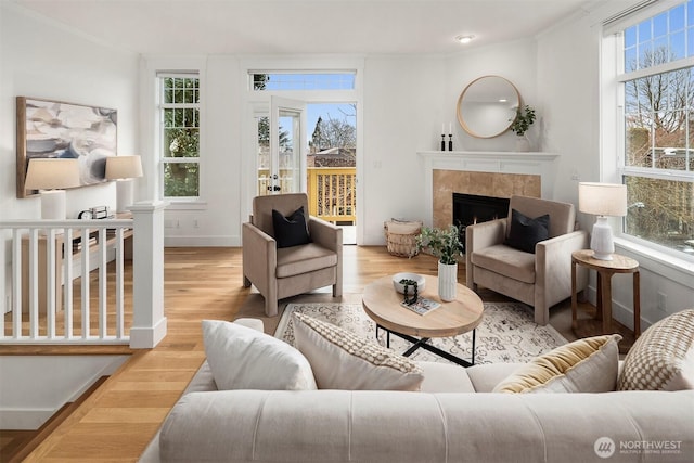 living area with baseboards, wood finished floors, crown molding, and a tile fireplace