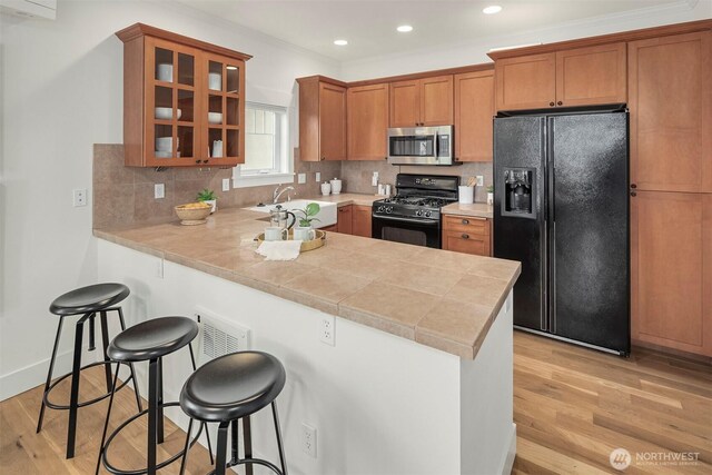 kitchen with a breakfast bar area, black appliances, light wood-style flooring, and a sink