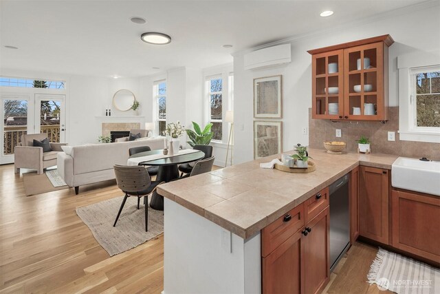 kitchen with light wood-style flooring, a fireplace, glass insert cabinets, a wall mounted air conditioner, and dishwasher