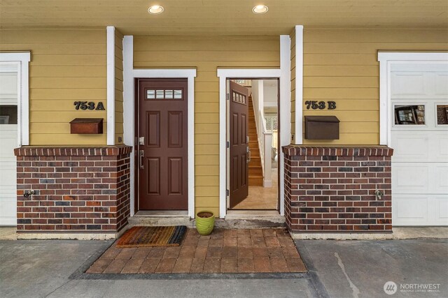 view of exterior entry featuring a porch, brick siding, and a garage