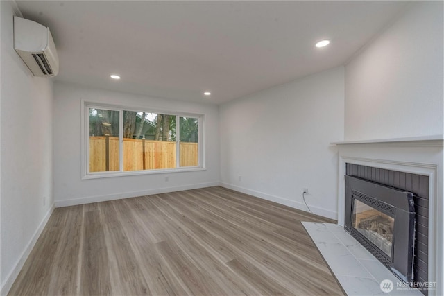 unfurnished living room with a fireplace, a wall mounted AC, baseboards, and wood finished floors