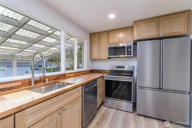 kitchen with light brown cabinets, a sink, butcher block countertops, light wood-style floors, and appliances with stainless steel finishes