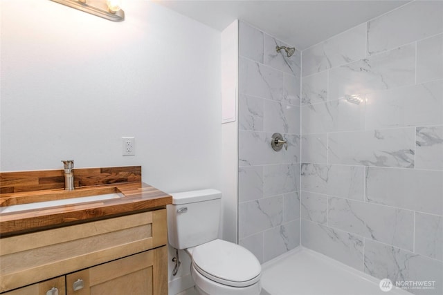 bathroom with toilet, vanity, and a tile shower