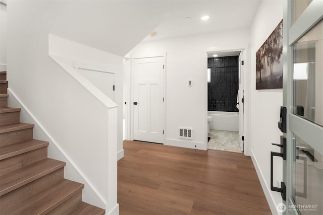 hallway featuring visible vents, wood finished floors, recessed lighting, baseboards, and stairs