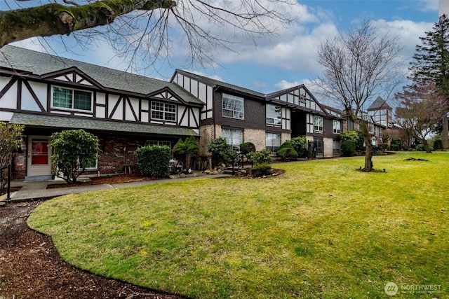 exterior space with a front lawn, brick siding, roof with shingles, and stucco siding