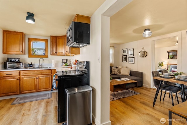 kitchen featuring a sink, light countertops, light wood-style floors, appliances with stainless steel finishes, and brown cabinets