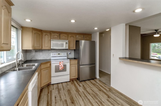 kitchen with a sink, white appliances, backsplash, and light wood-style flooring