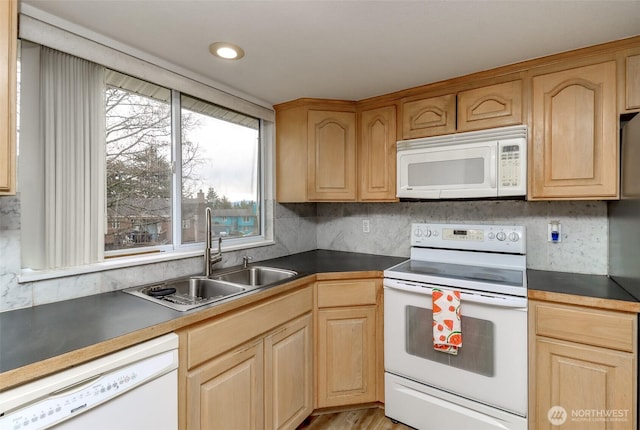 kitchen with light brown cabinetry, white appliances, dark countertops, and a sink