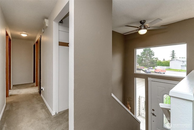 entryway with baseboards, light colored carpet, a ceiling fan, and a textured ceiling