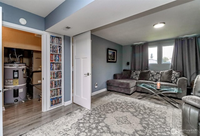 living room with secured water heater, wood finished floors, visible vents, and baseboards